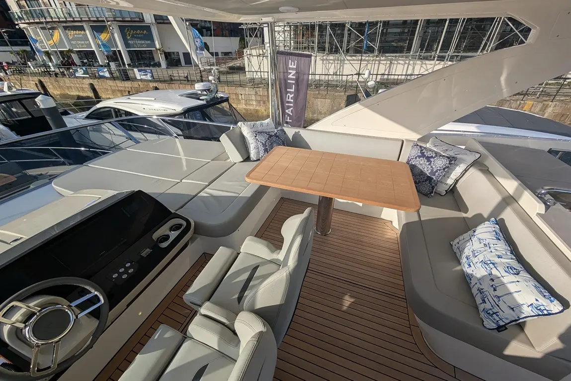 Luxury yacht cockpit featuring a wooden table, plush seating, and a modern helm with controls, set against a marina backdrop.